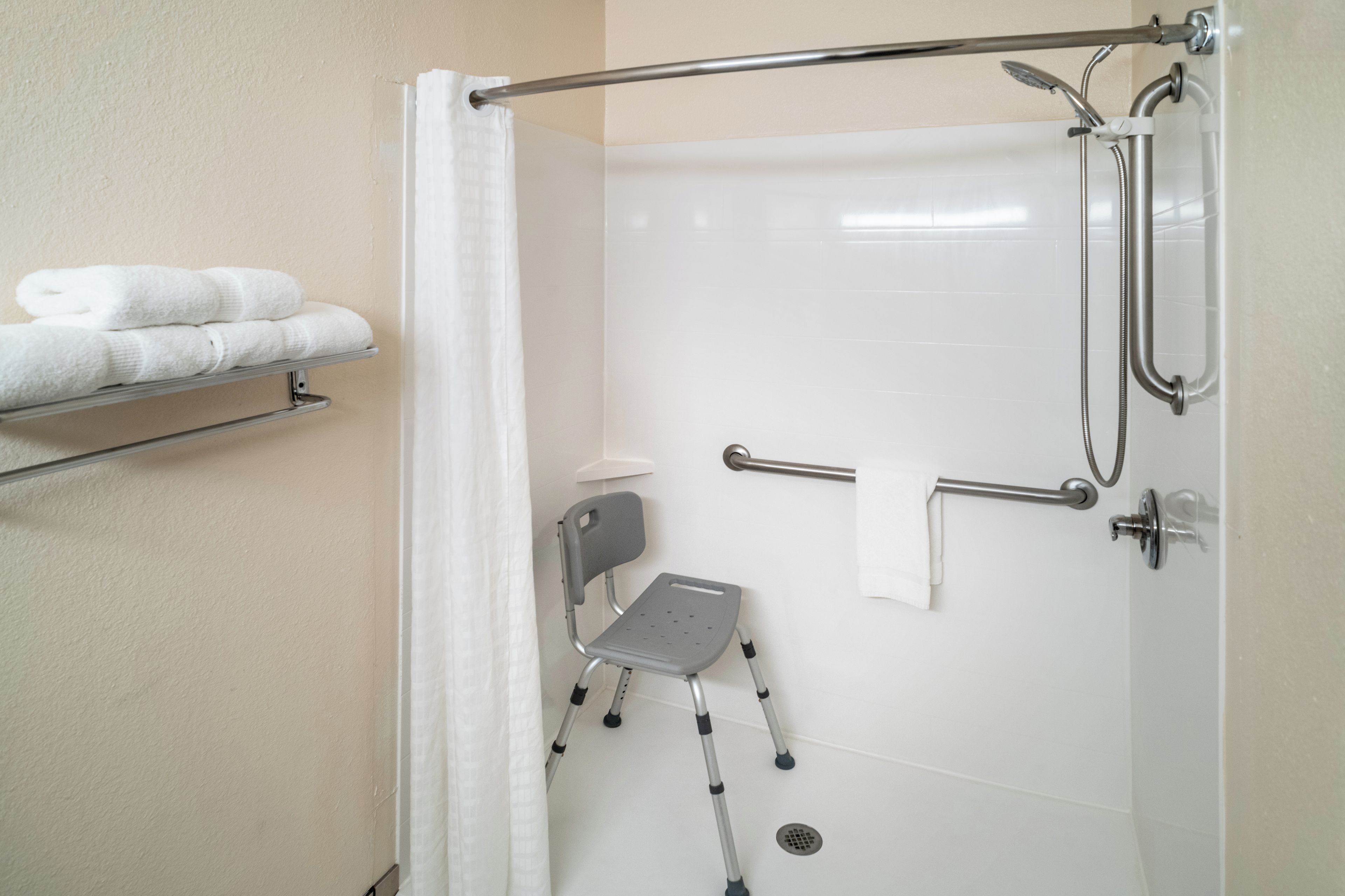 A shower area with a grab bar, a wheelchair, and a towel rack with folded towels.