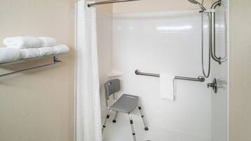 Un área de ducha con barra de apoyo, una silla de ruedas y un perchero con toallas dobladas.