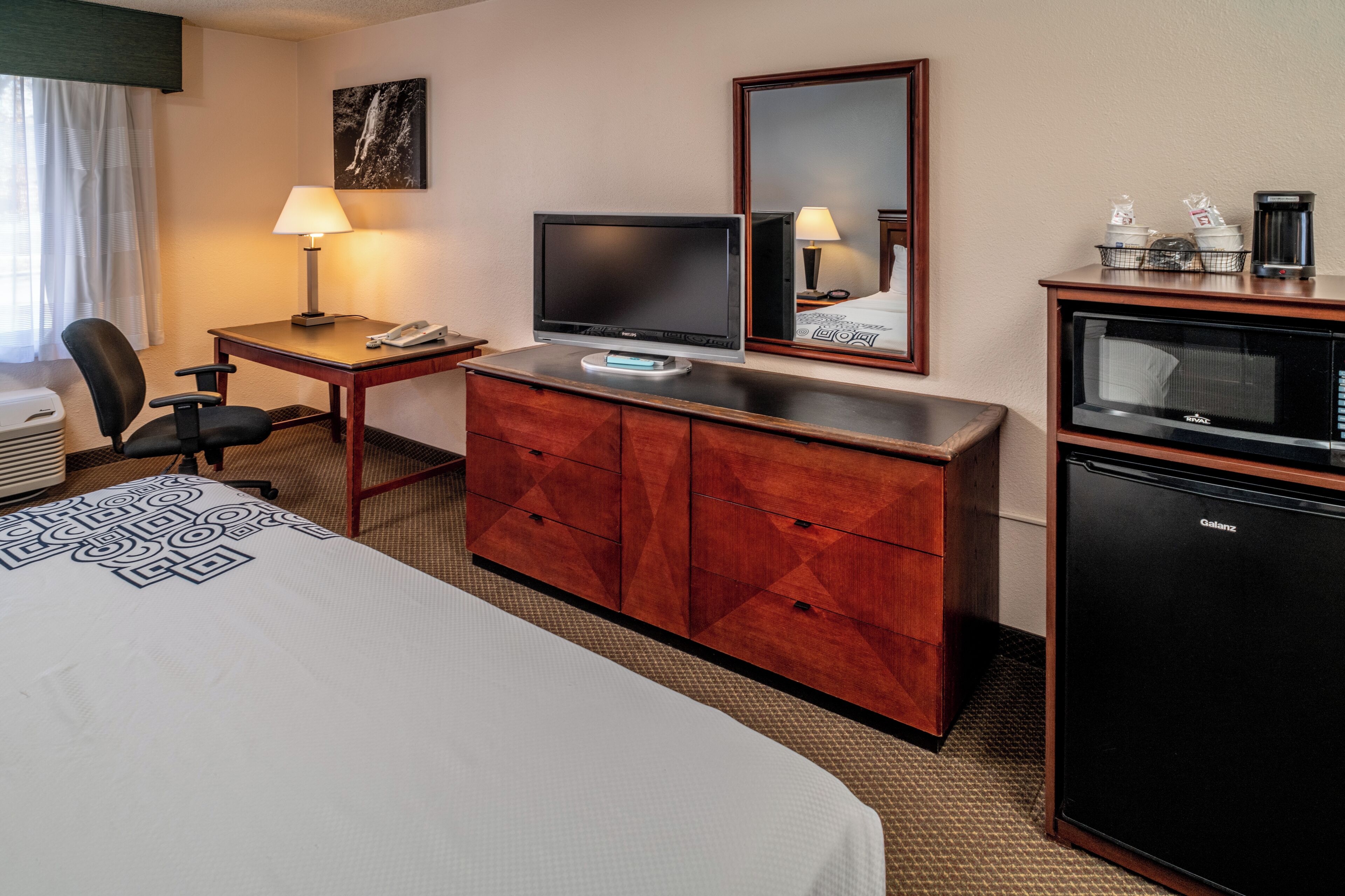Une chambre d’hôtel équipée d’un lit, d’un bureau, d’une chaise, d’une télévision, d’un four à micro-ondes et d’un petit réfrigérateur.