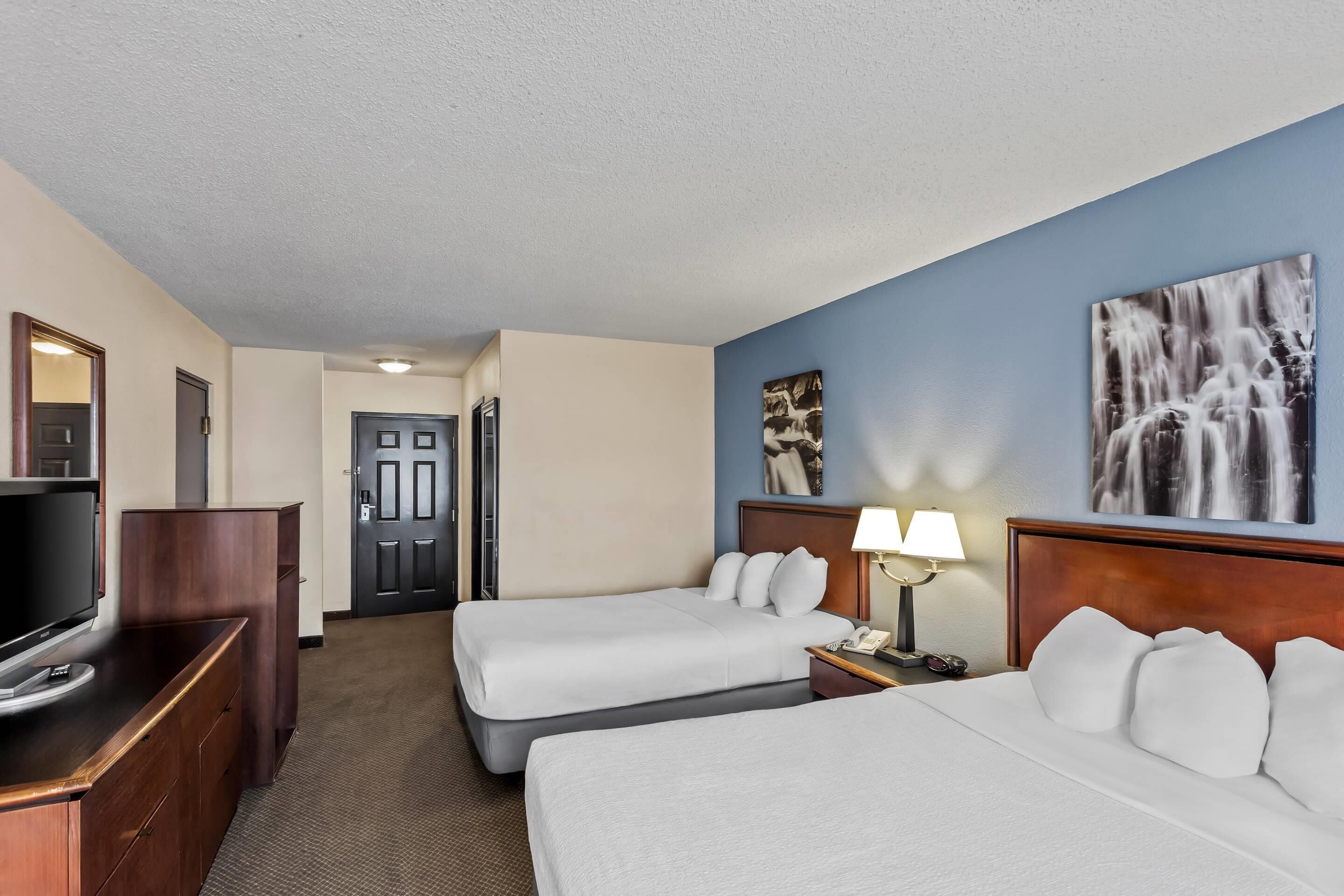 A hotel room with two beds, a TV, a desk, and artwork on the wall.