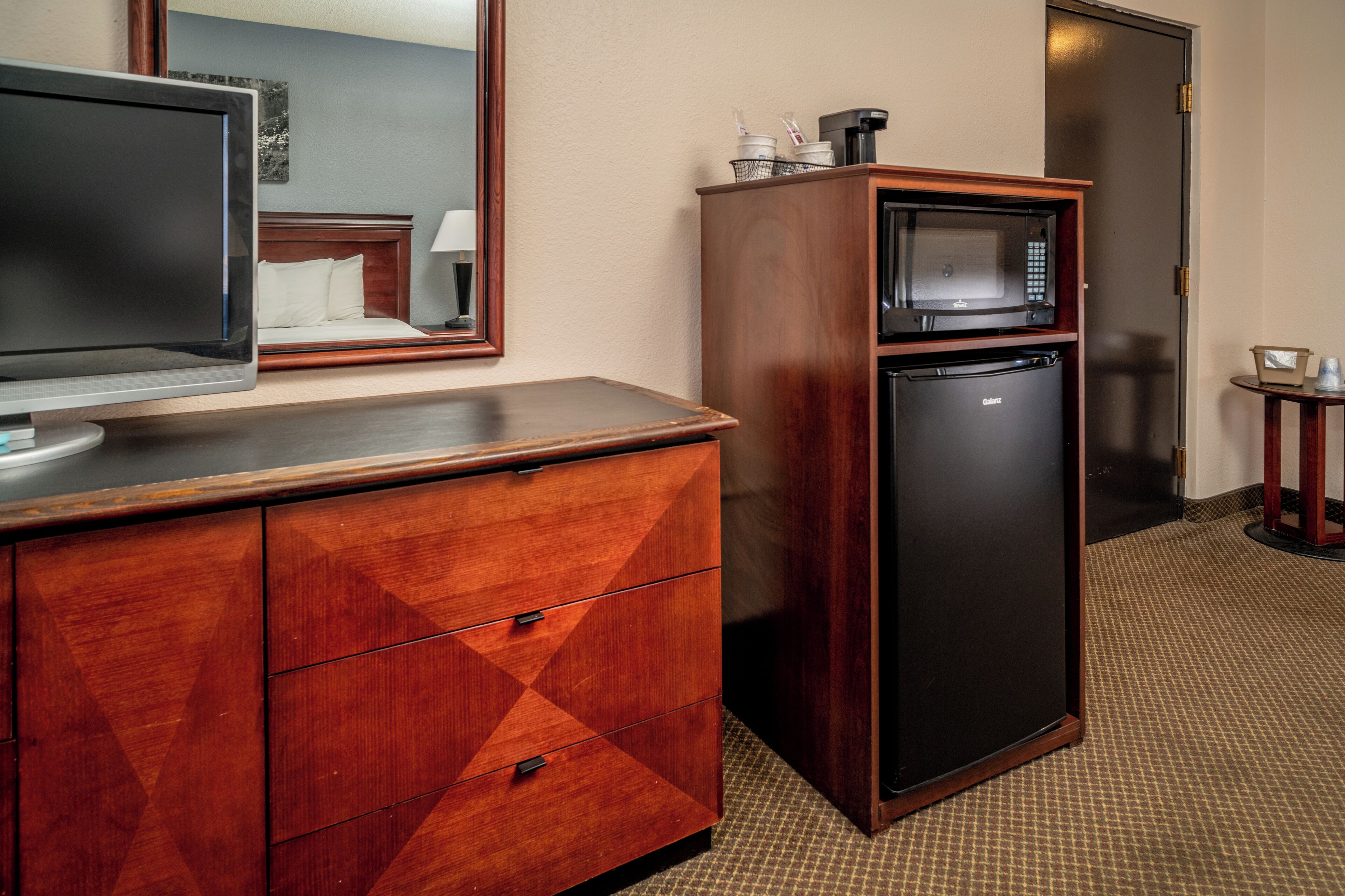 Een hotelkamer met een houten dressoir, een flatscreen-tv, een magnetron en een koelkast.