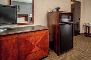 Une chambre d’hôtel équipée d’une commode en bois, d’un téléviseur à écran plat, d’un four à micro-ondes et d’un réfrigérateur.