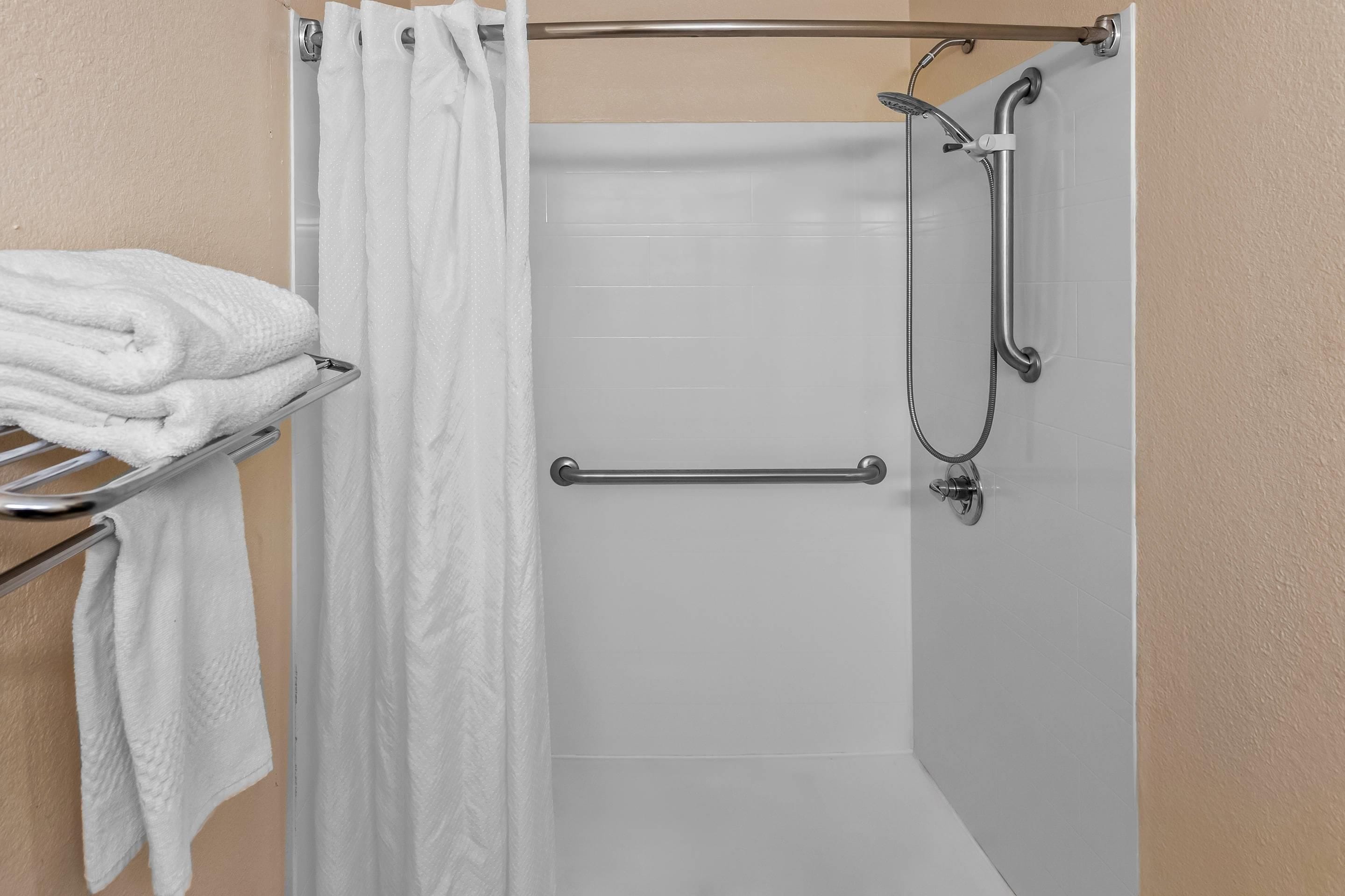 Une salle de bain avec une douche, un porte-serviettes avec des serviettes pliées et une barre d’appui.