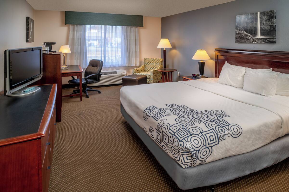 A hotel room with a bed, desk, chair, television, and lamps.