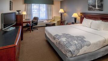 A hotel room with a bed, desk, chair, television, and lamps.