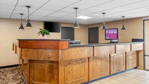 A reception desk with a wooden finish, a potted plant, a flat-screen monitor, and pendant lighting. - Rodeway Inn (Barboursville)