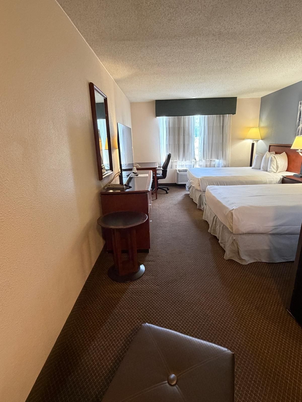 A hotel room with a desk, two beds, a chair, a small table, and a sofa.