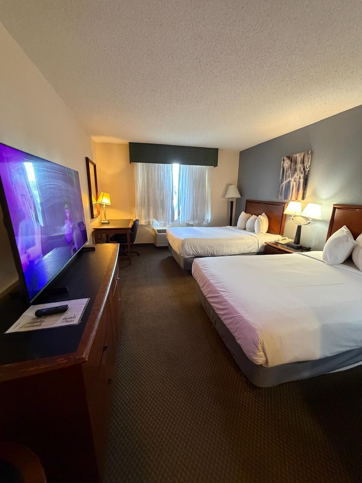Une chambre d’hôtel équipée d’une télévision, de deux lits, d’un bureau et d’une fenêtre avec des rideaux.