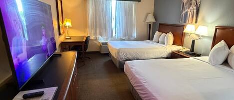 Une chambre d’hôtel équipée d’une télévision, de deux lits, d’un bureau et d’une fenêtre avec des rideaux.