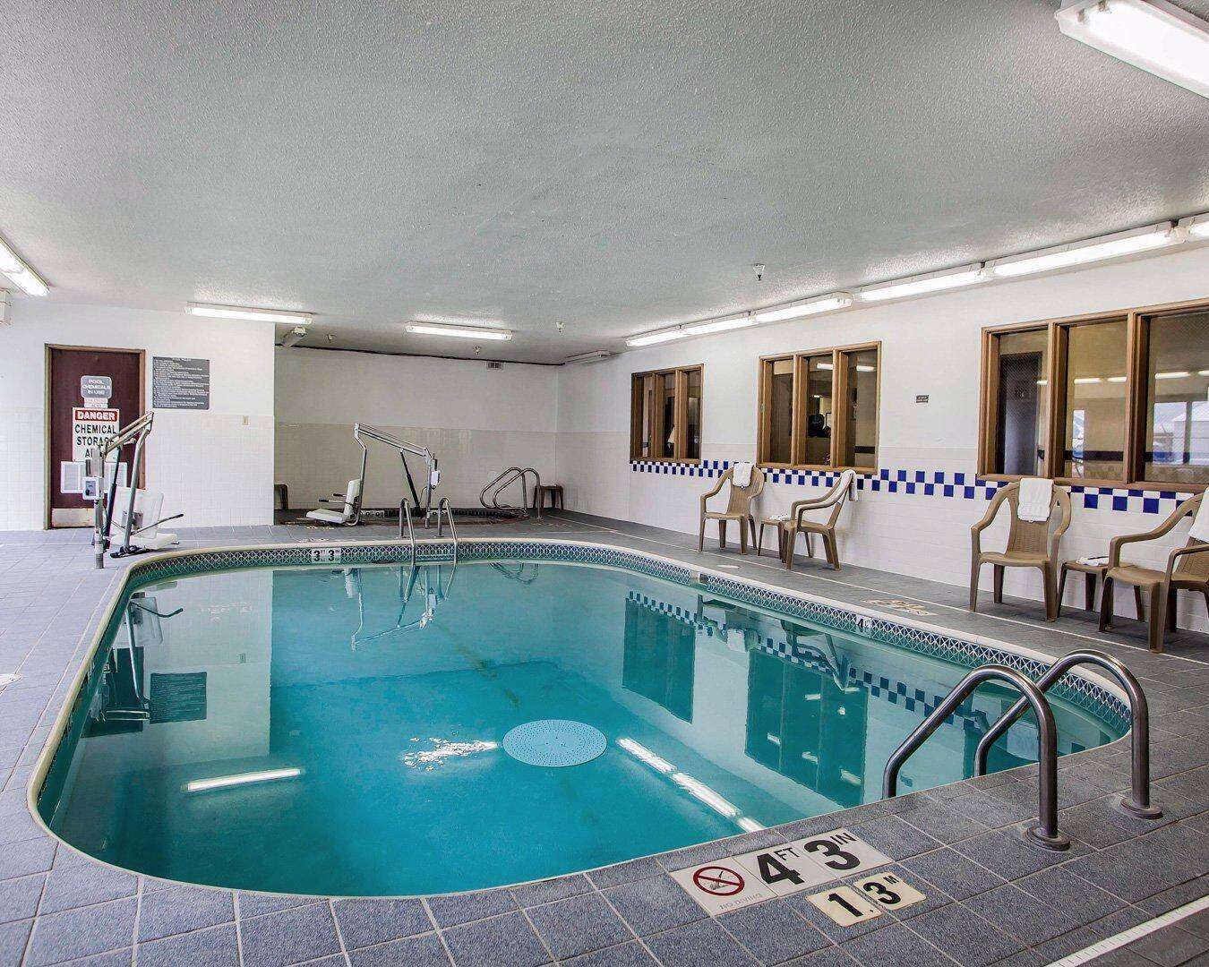 An indoor swimming pool with clear water, safety signs, and a tiled floor.