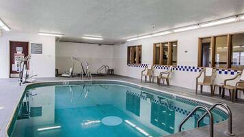 An indoor swimming pool with clear water, safety signs, and a tiled floor.