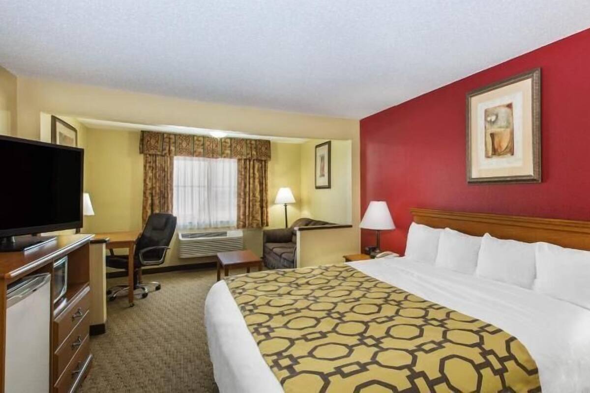 A hotel room with a bed, a desk, a television, a chair, and a window with curtains.