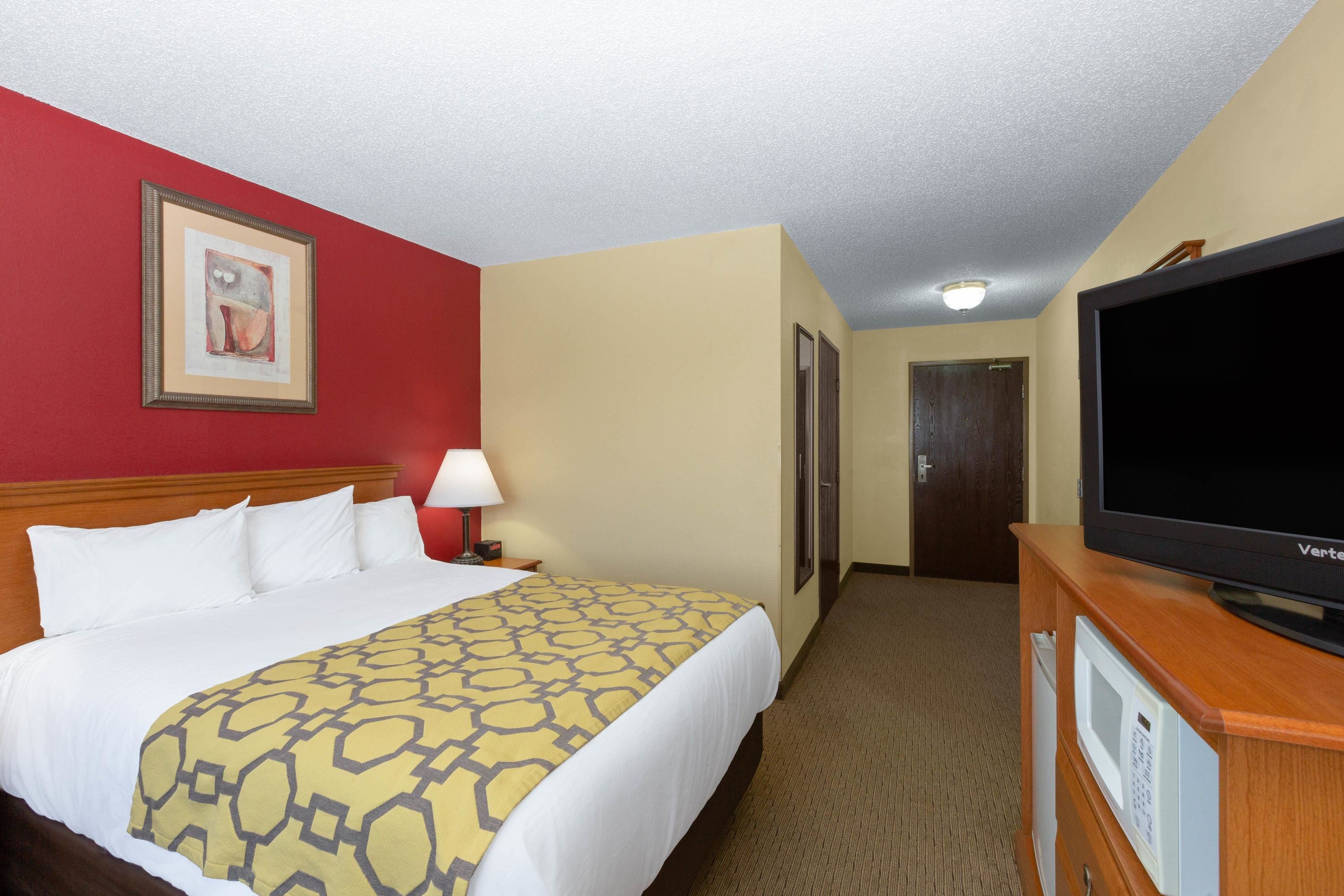 A hotel room with a bed, a television, a lamp, and a door.