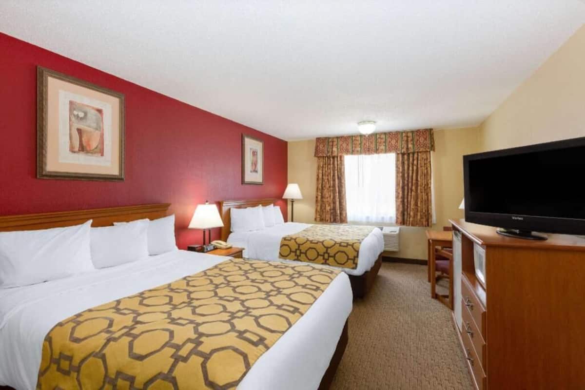 A hotel room with two beds, a television, a desk, and a window with curtains.