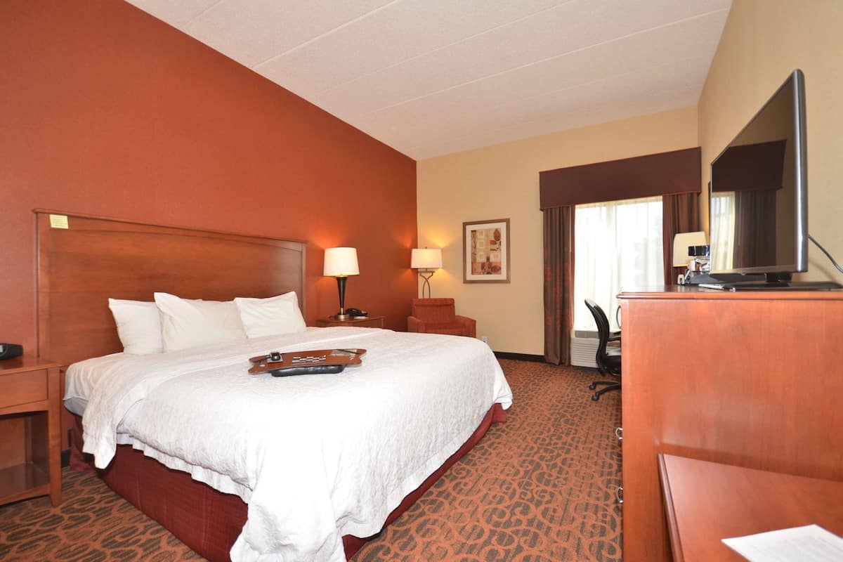 A hotel room with a large bed, a desk, a chair, a TV, and a lamp.