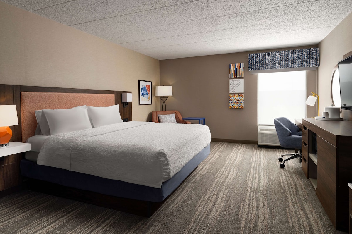 A hotel room with a bed, desk, chair, and artwork on the walls.