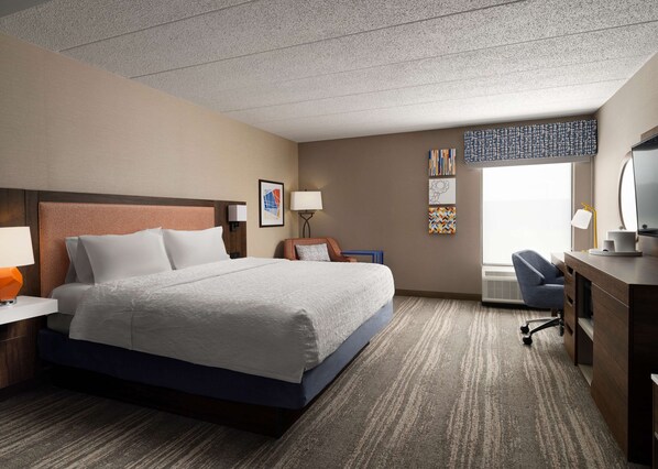 Habitación de hotel con cama, escritorio, silla y obras de arte en las paredes.