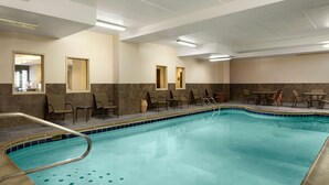Una piscina con borde de azulejos, sillas de descanso y mesas dispuestas alrededor de la zona de la piscina.