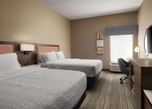 A hotel room with two large beds, a desk with a chair, a television, and artwork on the walls.