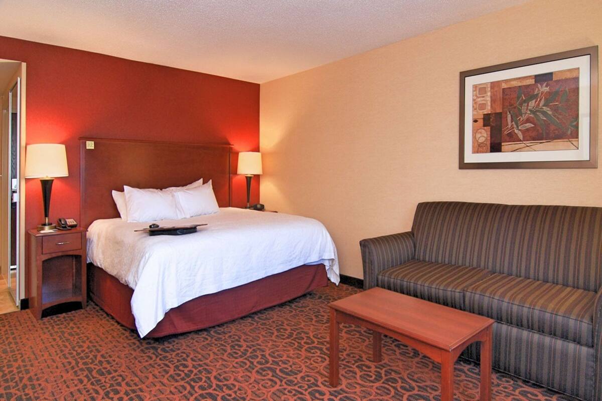 Una habitación de hotel con cama, dos lámparas de noche, un sofá, una mesita y una alfombra estampada.