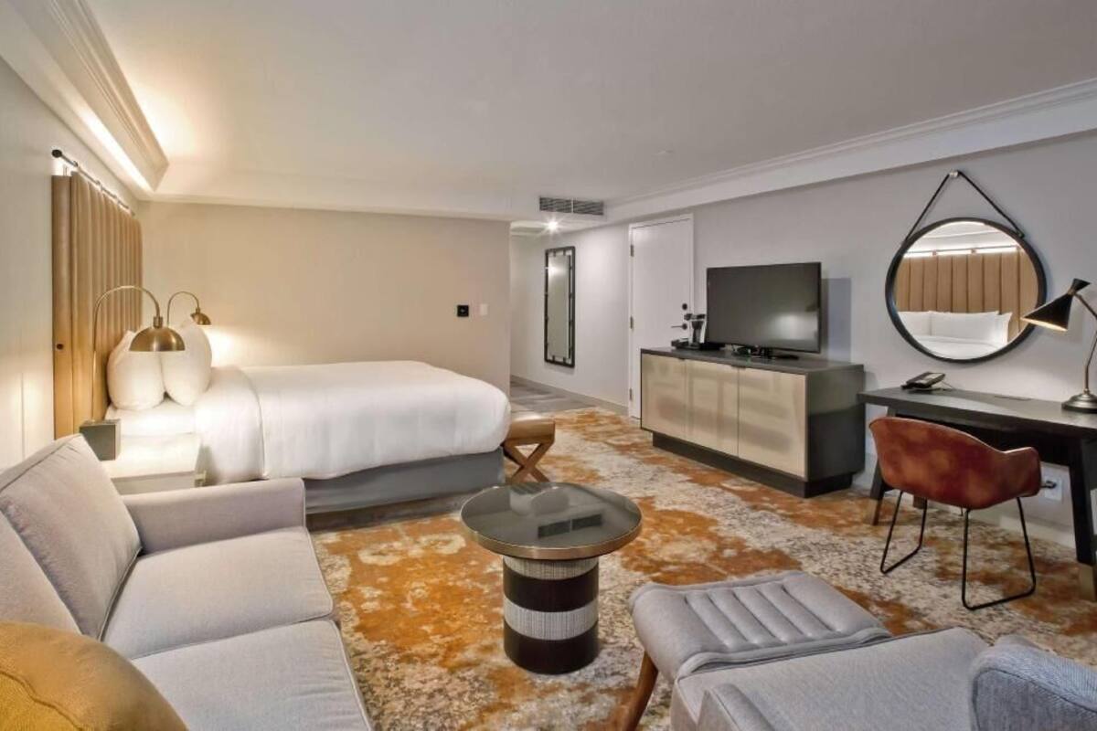 A hotel room with a bed, a sofa, a desk, a television, and a mirror.