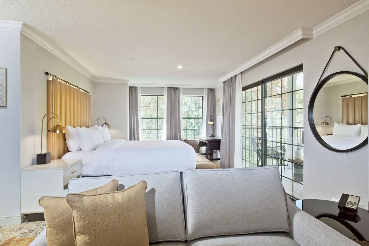 A hotel room with a large bed, a sofa, a desk, and a mirror.