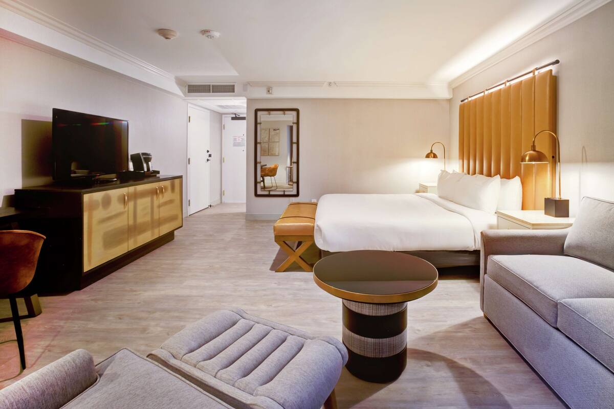 A modern hotel room with a bed, a sofa, a TV, a desk, and a small table.