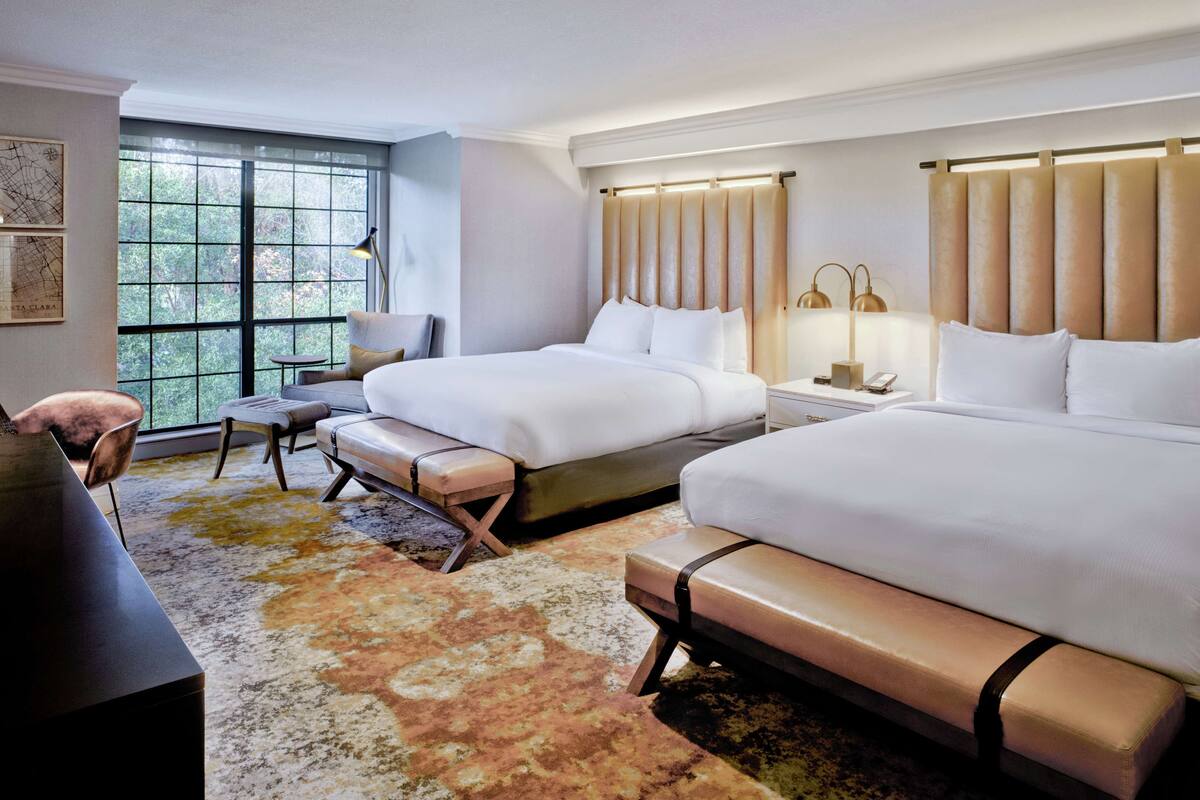 A hotel room with two beds, a desk, a chair, and a large window.