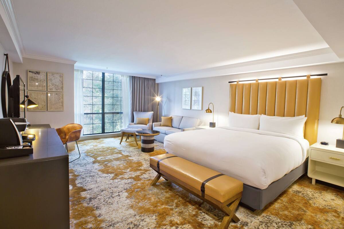 A modern hotel room with a large bed, a desk, a sofa, and a coffee table.