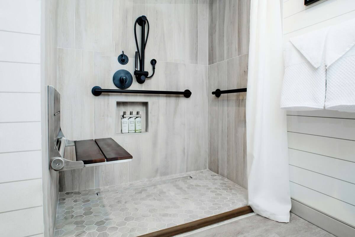 A shower area with a wooden bench, a towel rack, and a shelf with toiletries.