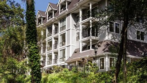 A multi-story hotel with balconies, surrounded by lush greenery and a small stream. - The Inn at Saratoga, Tapestry Collection by Hilton (Saratoga)