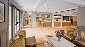A spacious hotel lobby with a modern design, featuring a central seating area with leather sofas, a coffee table, and a vase of flowers. - The Inn at Saratoga, Tapestry Collection by Hilton (Saratoga)