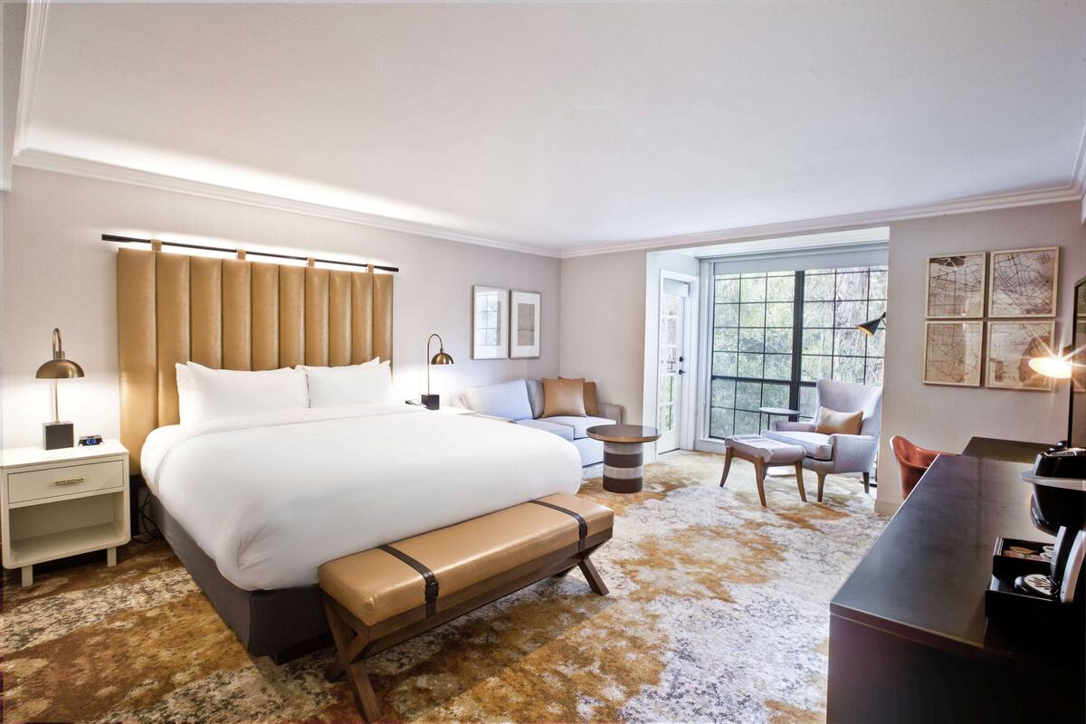 A hotel room with a large bed, a desk, a chair, a sofa, and a window with a view.