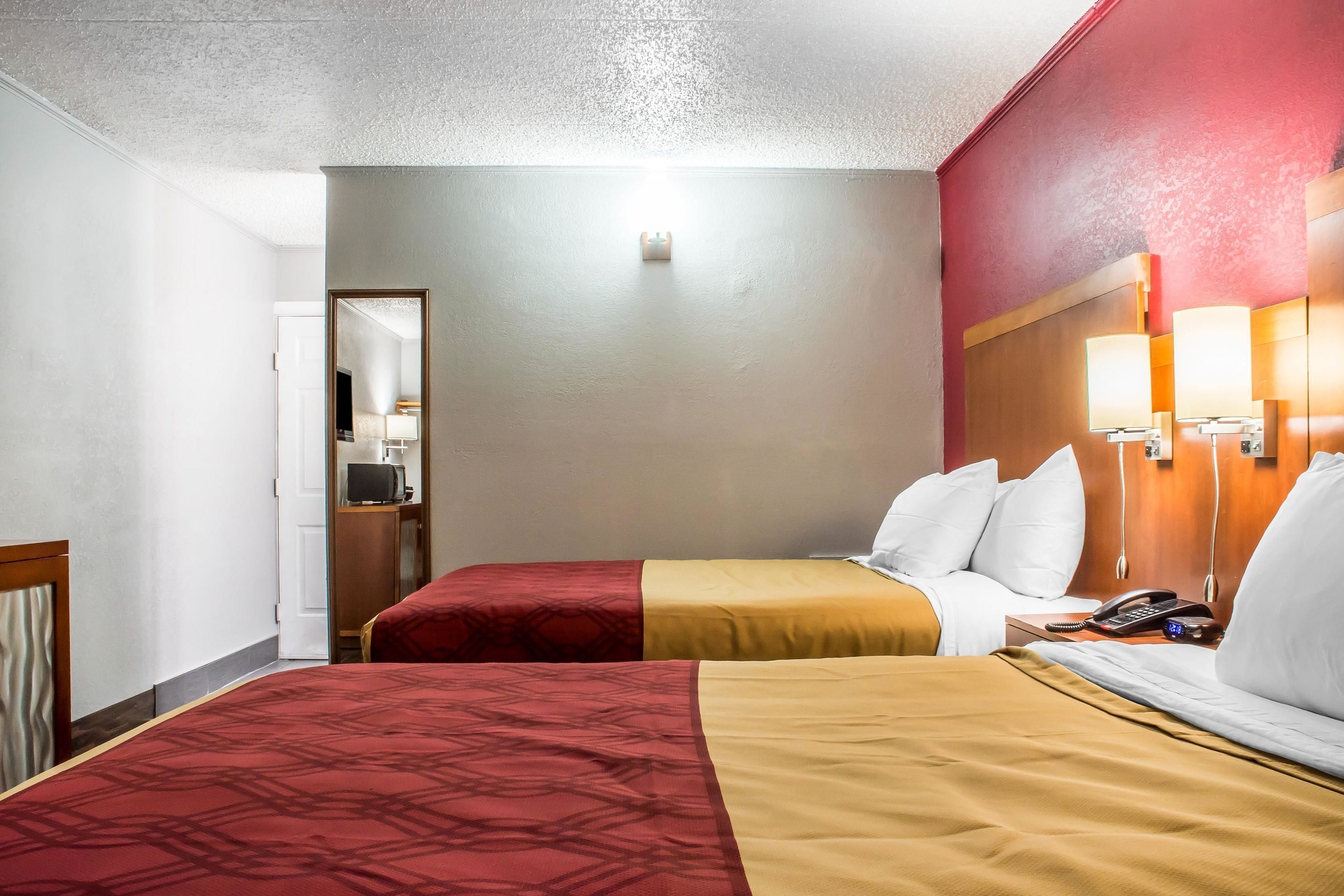 Une chambre d’hôtel avec deux lits, une tête de lit en bois, des lampes de chevet, un téléphone et un miroir.