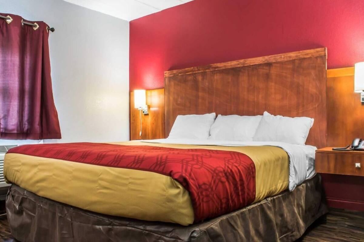 A hotel room with a bed, a wooden headboard, a nightstand with a phone, and a red wall.