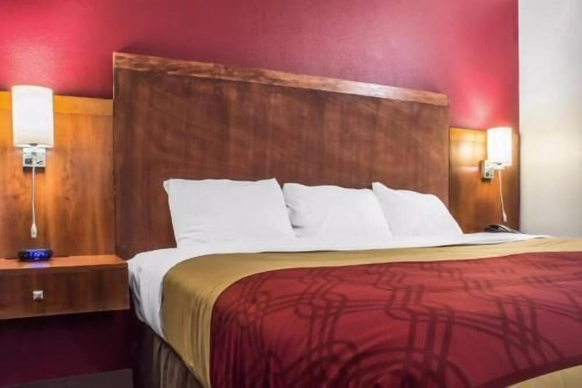 A hotel room with a wooden headboard, white bedding, and two bedside lamps.