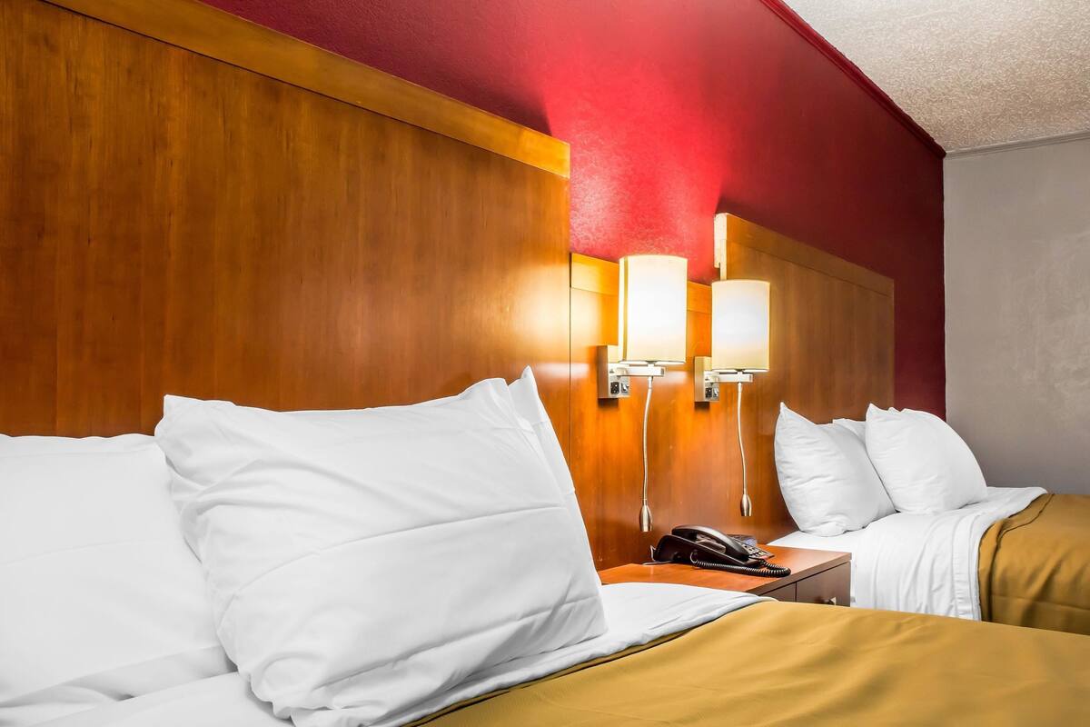 A hotel room with two beds, wooden headboard, bedside lamps, a telephone, and a nightstand.