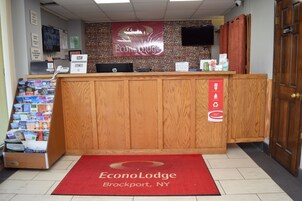 Un mostrador de recepción con alfombra roja, pared de piedra y un letrero de EconoLodge en Brockport, NY.