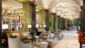 A spacious lobby with a high ceiling, ornate columns, and a chandelier. There are seating areas with sofas and armchairs, and a large bookshelf filled with books and decorative items. - The Westin Palace, Milan (Milan)