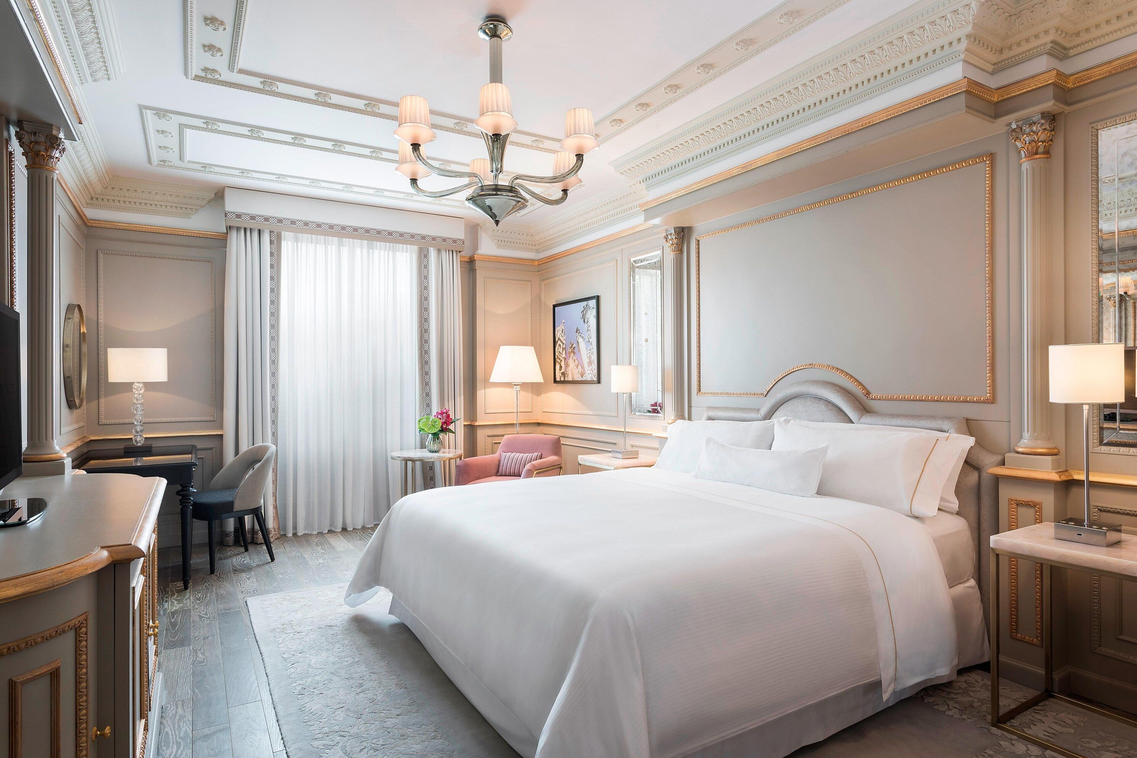 A hotel room with a large bed, a desk, a chair, and a chandelier.