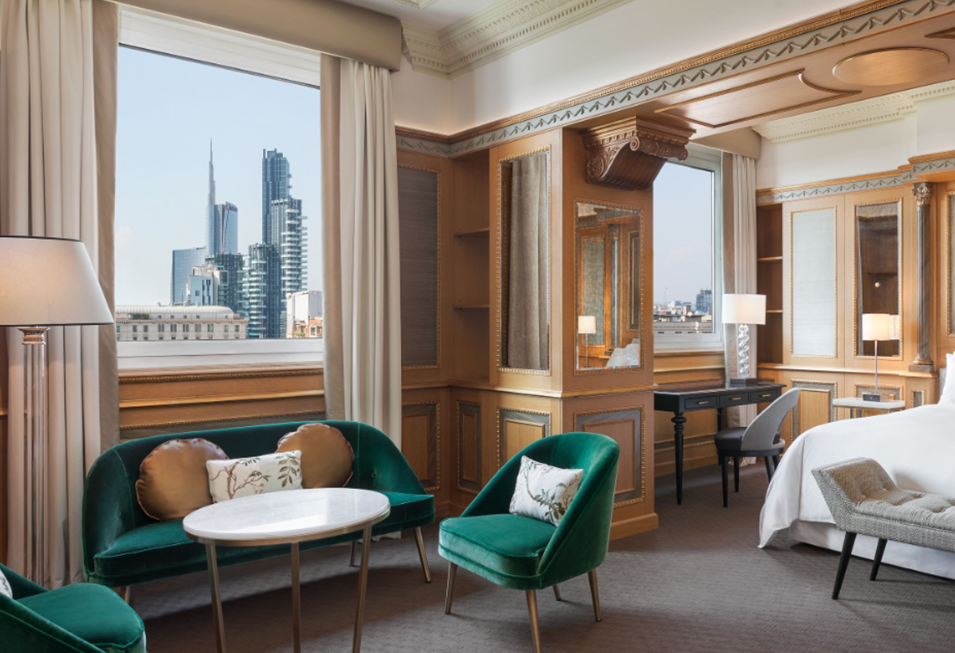 Ein Hotelzimmer mit Blick auf die Stadt, einem Schreibtisch, einem Bett und zwei grünen Sesseln.