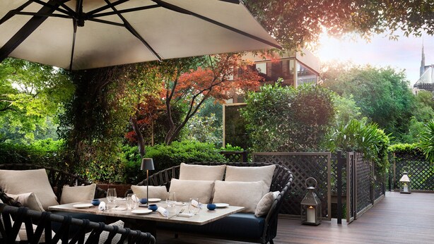An outdoor dining area with a table set for two, surrounded by wicker chairs and a cushioned bench. - The Westin Palace, Milan (Milan)