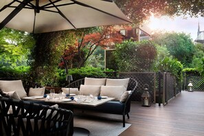 An outdoor dining area with a table set for two, surrounded by wicker chairs and a cushioned bench. - The Westin Palace, Milan (Milan)