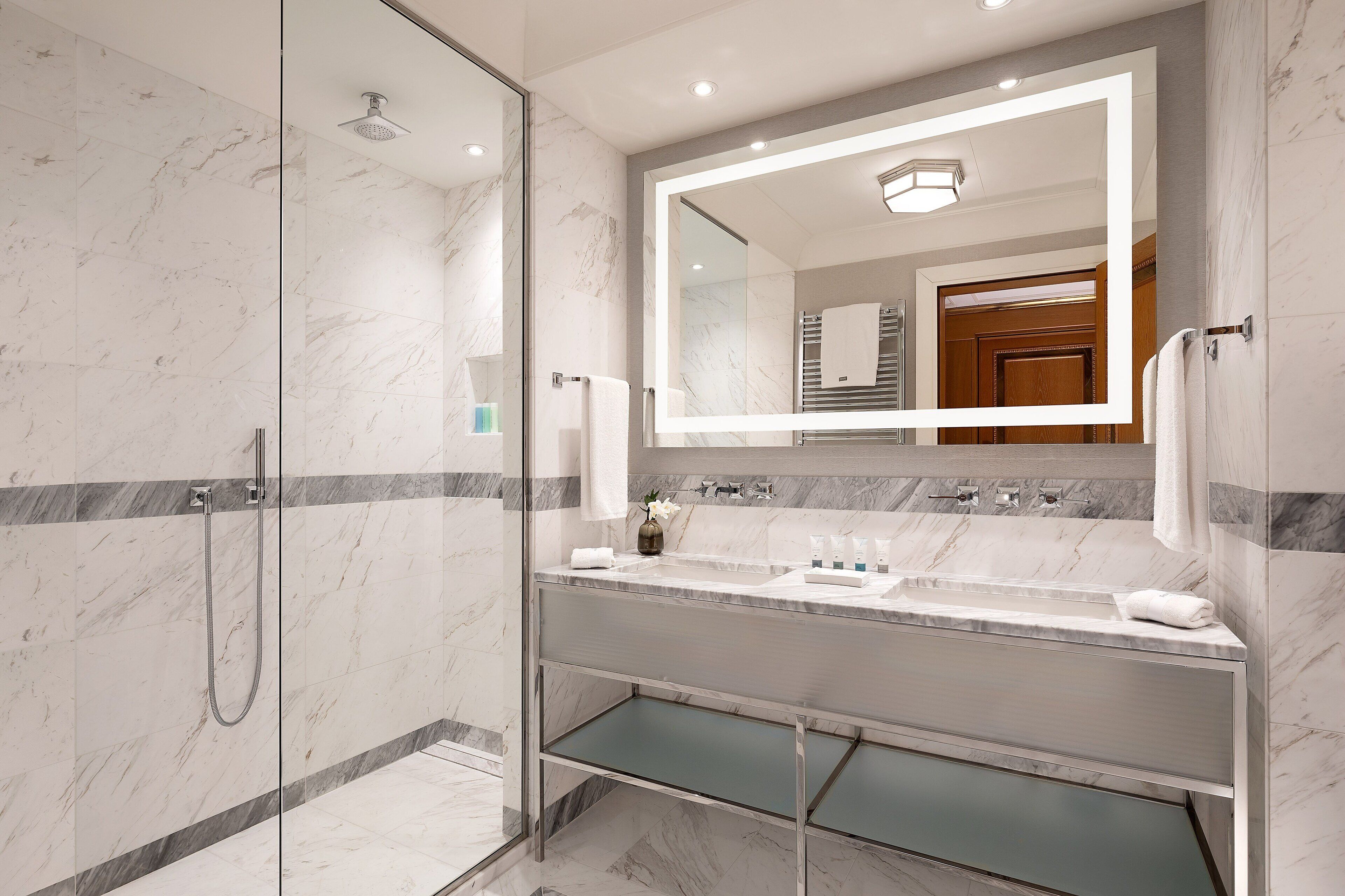 Ein modernes Badezimmer mit einer Glaskabine zur Dusche, einem Waschtisch mit großem Spiegel und Marmorböden.