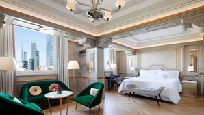 A luxurious hotel room with a large bed, a green armchair, a small round table, and a view of the city skyline. - The Westin Palace, Milan (Milan)