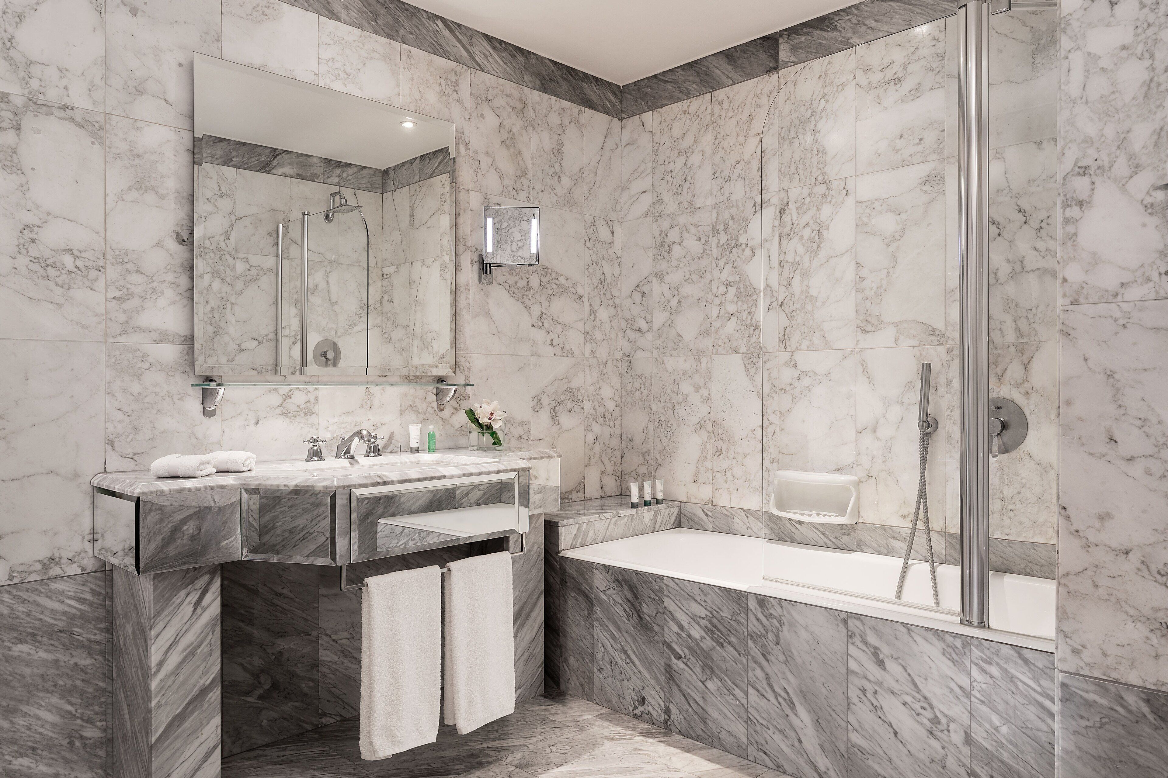 Une salle de bain moderne avec un mur en marbre, un grand miroir, une baignoire et un espace douche.