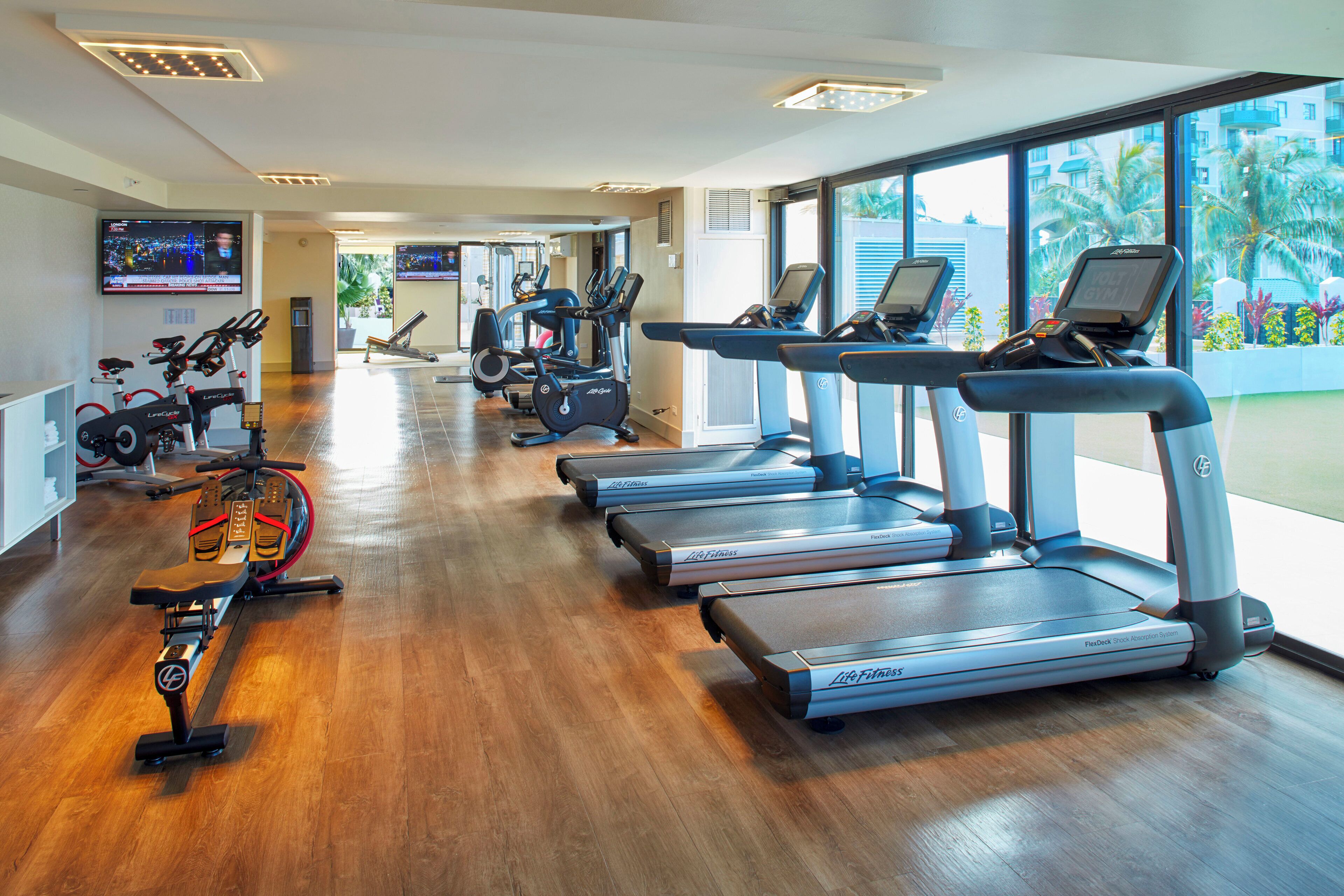 Un gimnasio con cintas de correr, bicicletas estáticas y una máquina de remo.