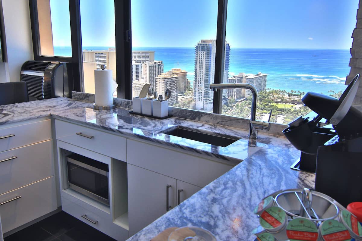 A kitchen with a view of the ocean and cityscape, featuring a marble countertop, modern appliances, and a built-in oven.