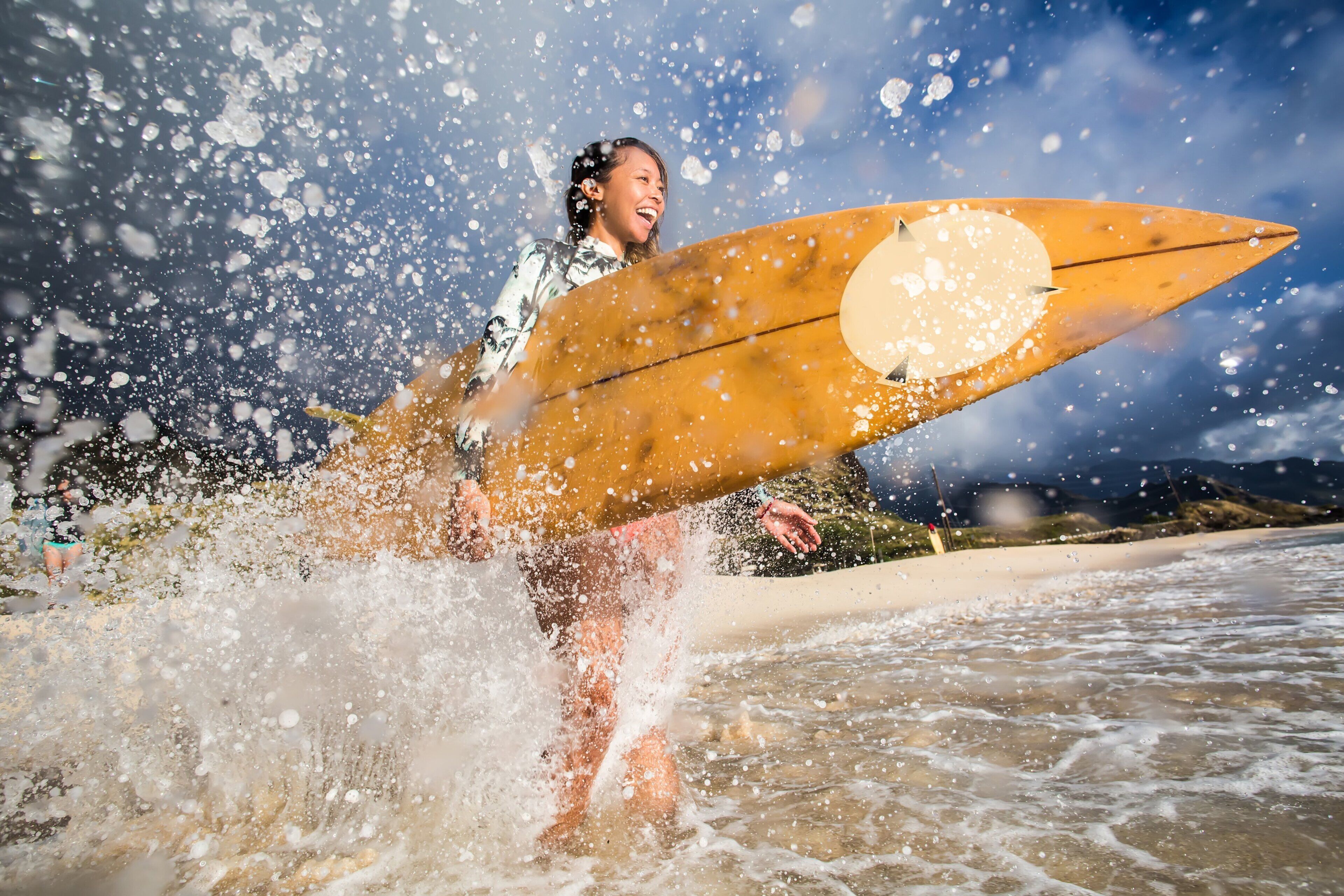 Una persona sosteniendo una tabla de surf con un diseño circular, de pie en el agua con salpicaduras a su alrededor.