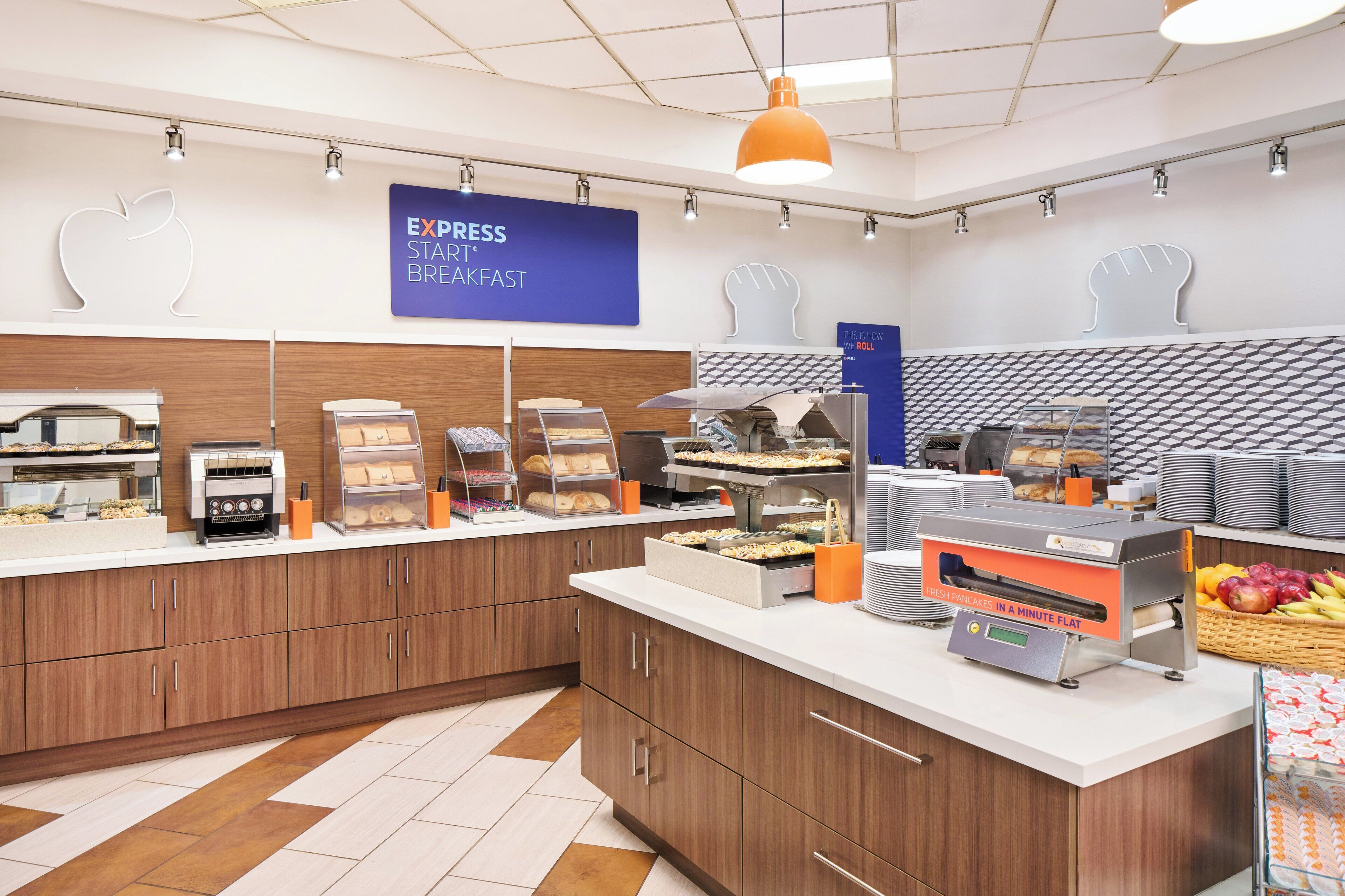 A breakfast area with a sign reading "EXPRESS START BREAKFAST," a toaster, a bread display, and a fruit basket.